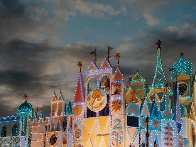An enchanting view of a fairy tale castle adorned with colorful lights against a dramatic evening sky