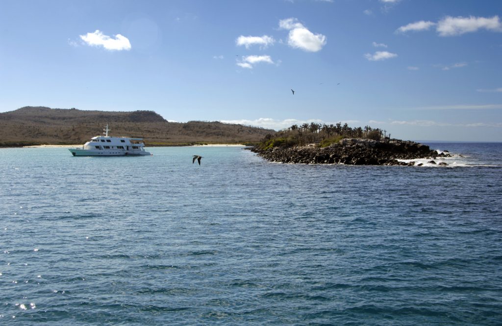 A sandy beach at Santa Fe Island, with black volcanic rock and a boat used for tours around the Galapagos Islands, Ecuador. 