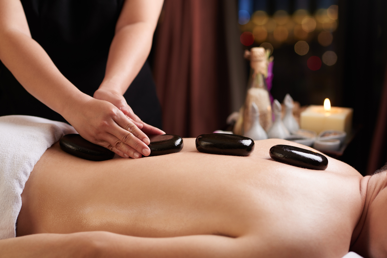 Masseur putting hot stones on the back of a visitor, self-care ideas