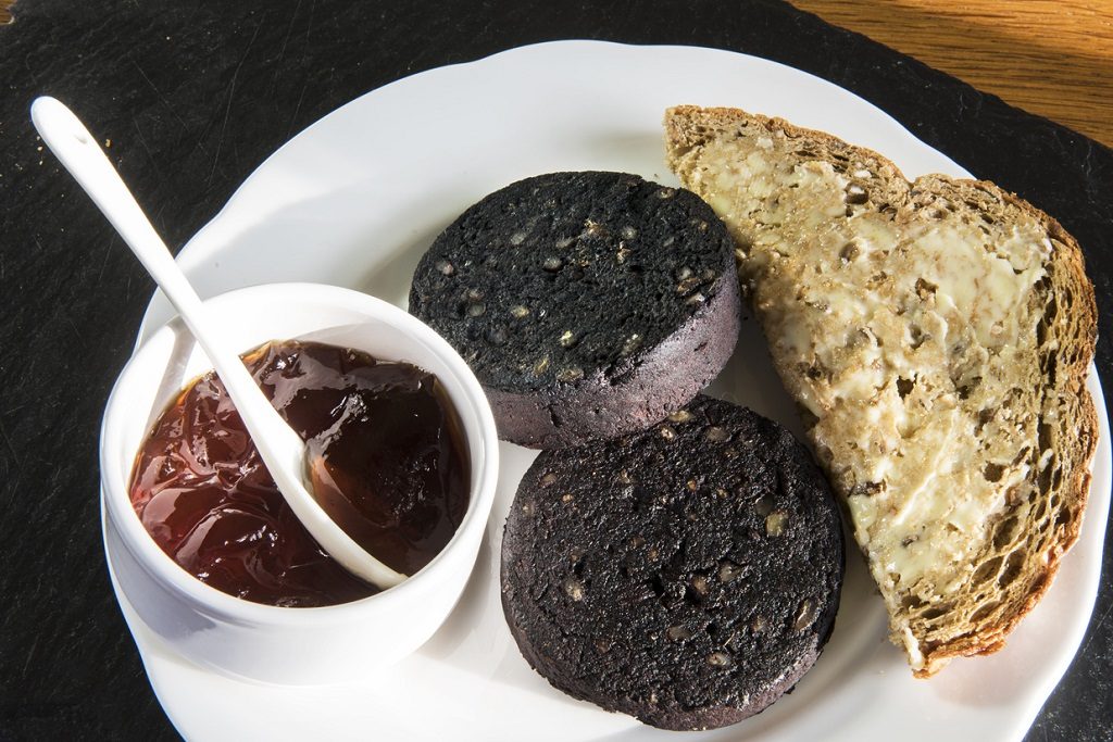 a portion of black pudding on a plate with bread and sauce