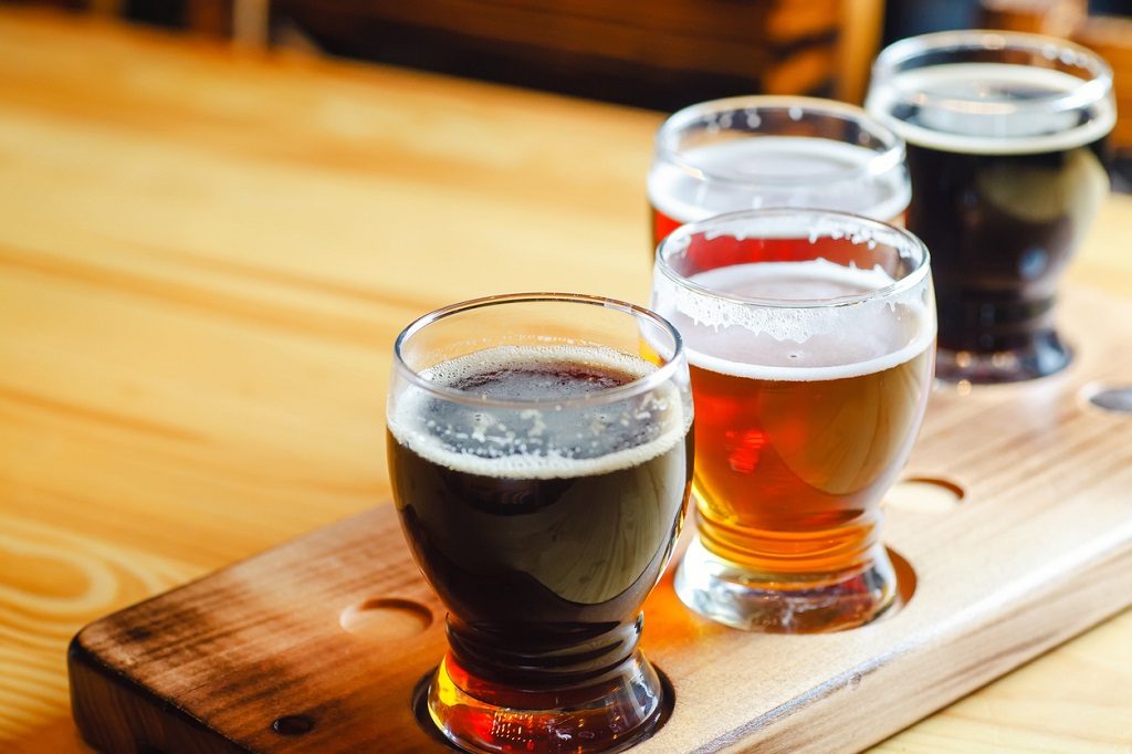 Flight with various types of craft beer in small glasses on a wooden table in a pub