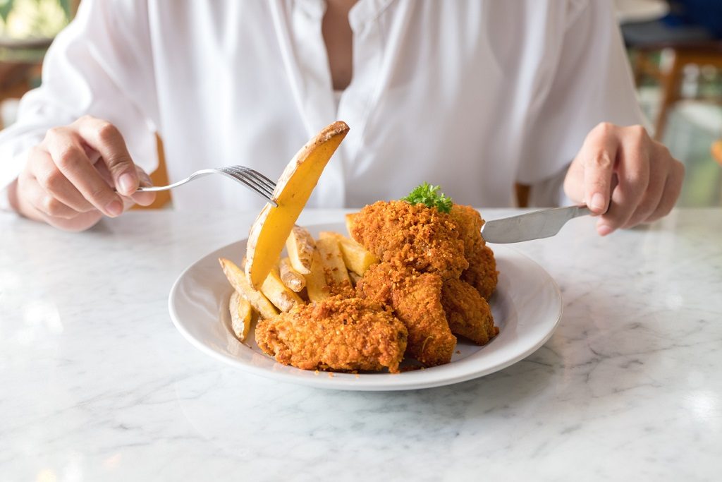 hands using knife and fork to eating french fries and fried chicken