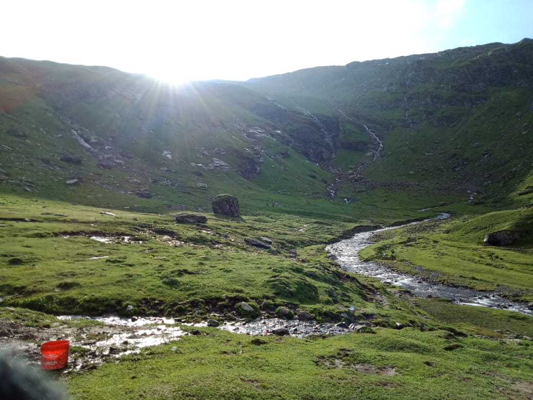 Sun shining on a grassy plain with a stream flowing through - trekking experiences