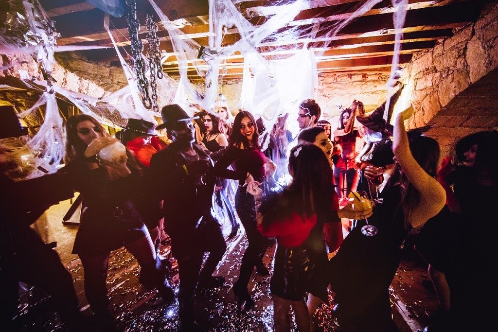 Young multi-ethnic friends dressed-up in Halloween costumes dancing and drinking at nightclub dungeon party