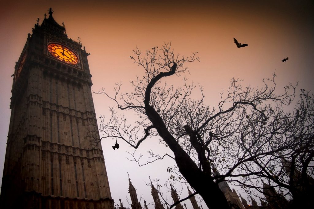 The spooky clock tower of Westminster with a bare tree and flying bats