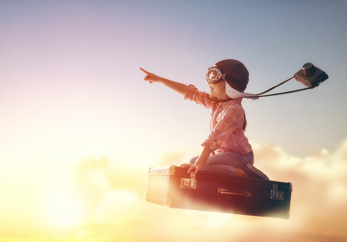 Child flying on a suitcase against the backdrop of a sunset