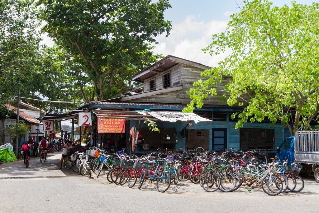 PULAU UBIN, SINGAPORE -March 11, 2016: Tourists ride past a shop with many bicycles for hire. Biking is the main mode of transportation on the island.