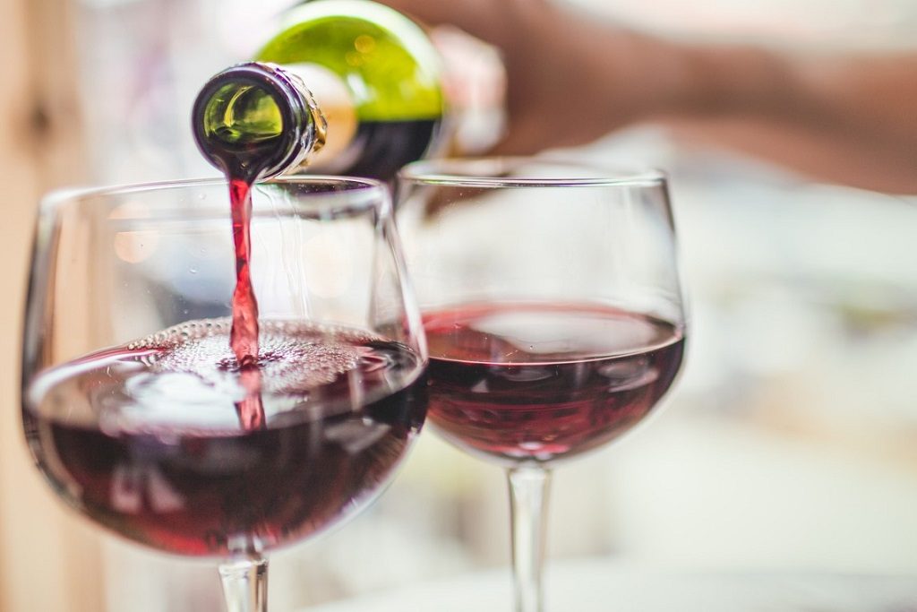 Unrecognizable man pouring red wine in two glasses. Drinking etiquette