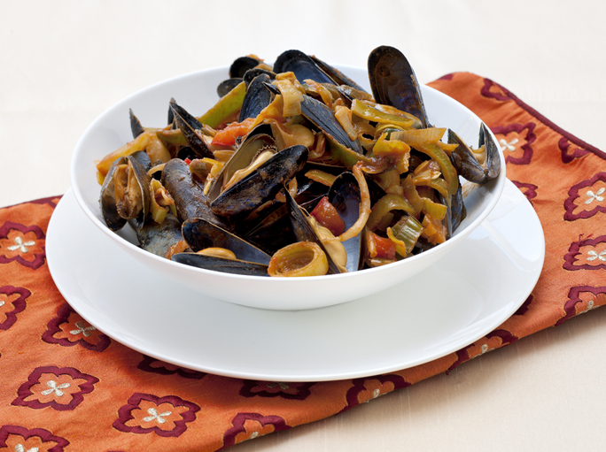 close up on a white bowl with sweet and sour boiled mussels and stir fried vegetables on table with napkin