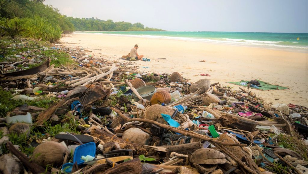 garbage on a beach left by tourist, environmental pollution concept picture. trash nailed by a wave from the sea on a beach. tourist resting on the beach near the big mountain of garbage, Overtourism