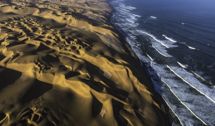 Aerial view of the sand dunes of the Namib Desert colliding with the Atlantic Ocean, Namibia.
