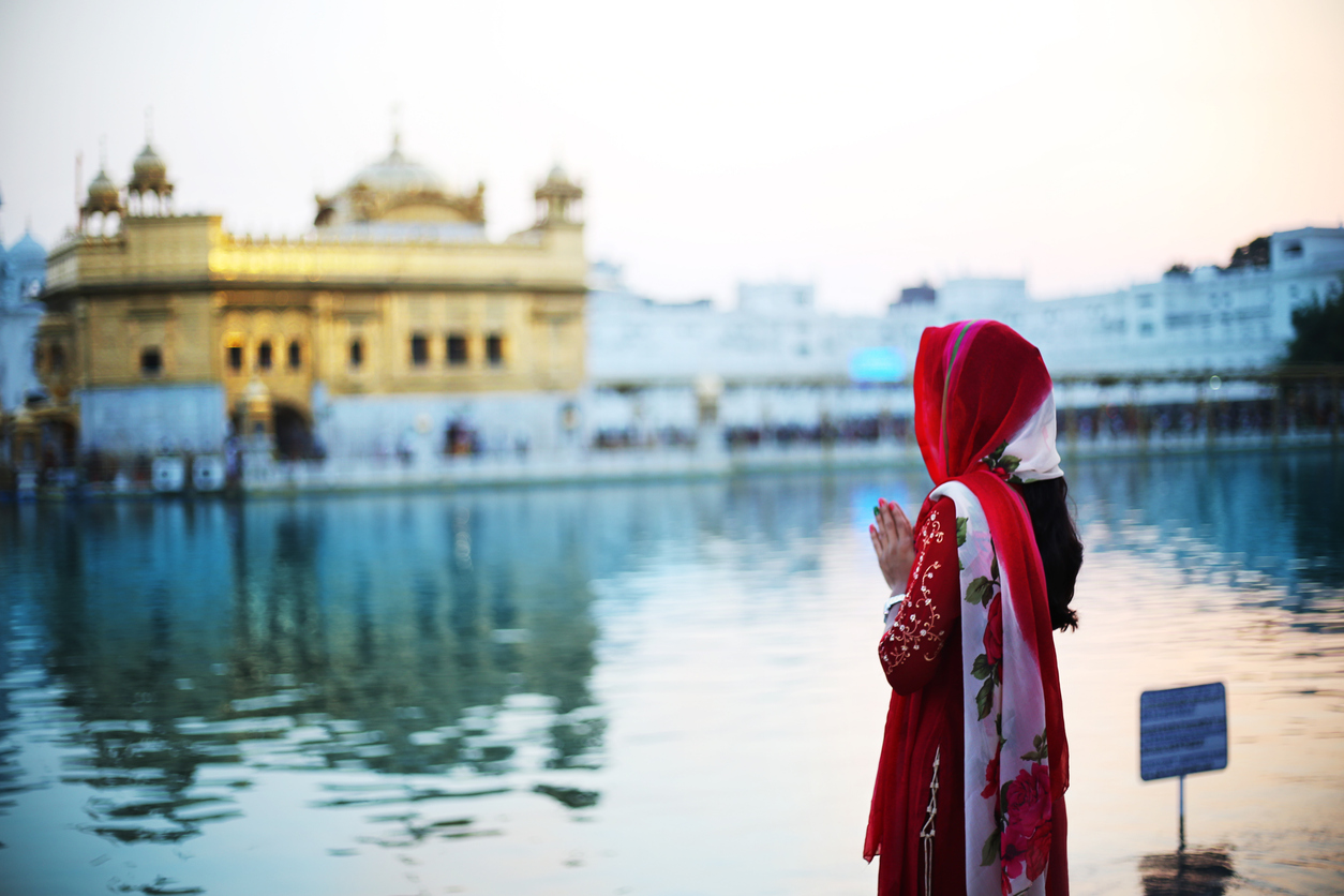 Young woman standing in front of the Golden Temple in Amritsar and praying, Punjab India, Religious Tourism