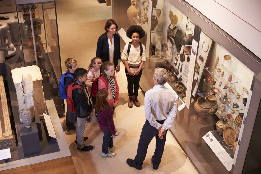 Students Looking At Artifacts In Case On Trip To Museum