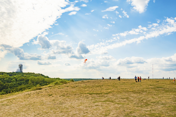 People who relax and observes other people, who let fly a kite on the "Teufelsberg" (devil hill) in Berlin, Germany. On the left side you can see an abandoned radar station.