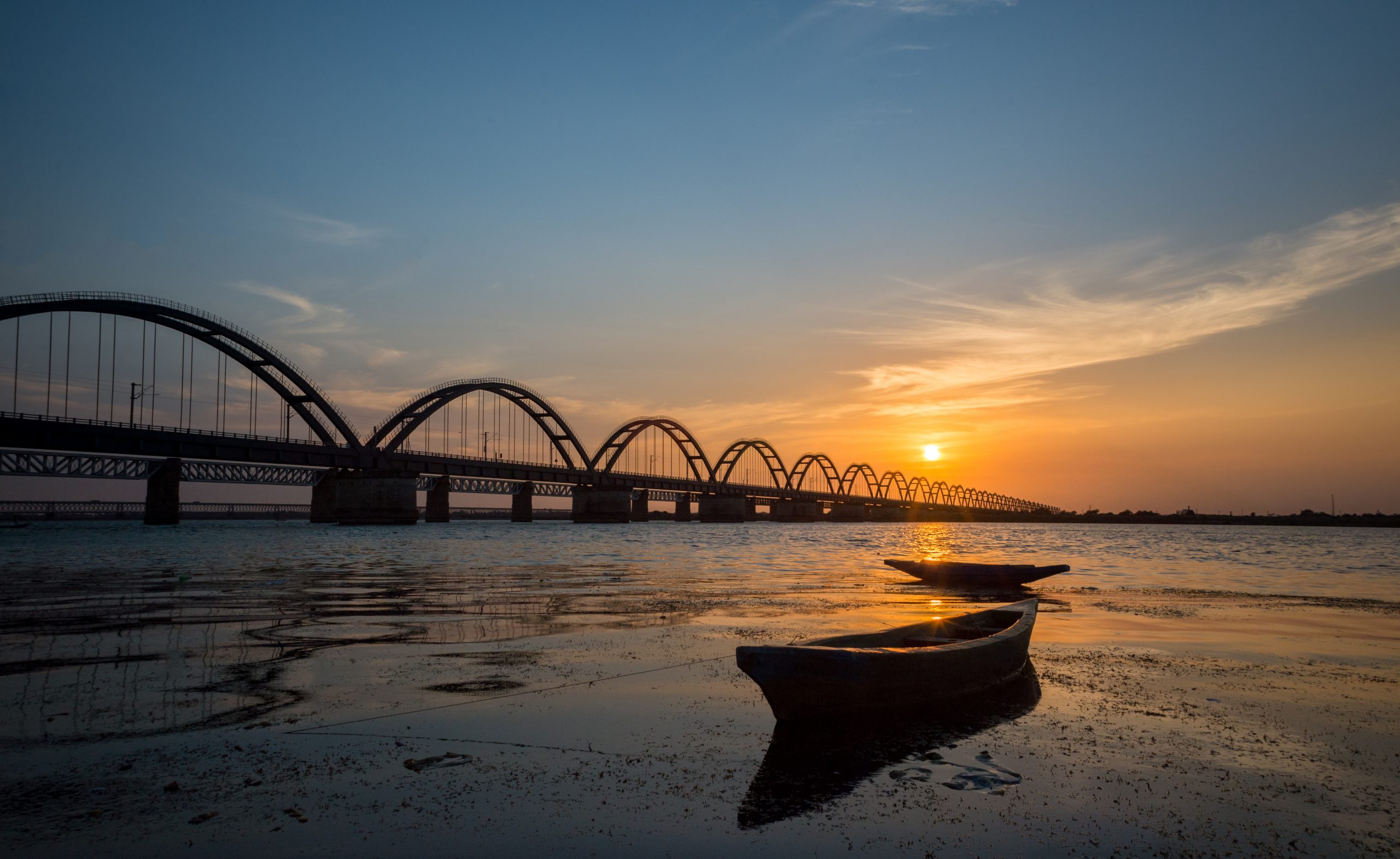 Sunset at Rajahmundry Pushkar ghat, andhra pradesh , in godawari river, with godawari old rail bridge view  with orange and blue colour sky and with boats in foreground