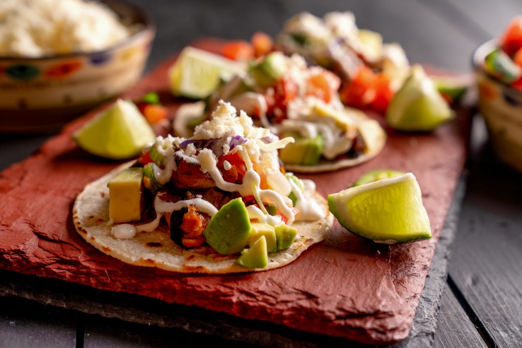 Pork Carnitas Tacos on a Rustic Slate Ready to be Served with Peppers, Lime, Salsa and Cotija Cheese