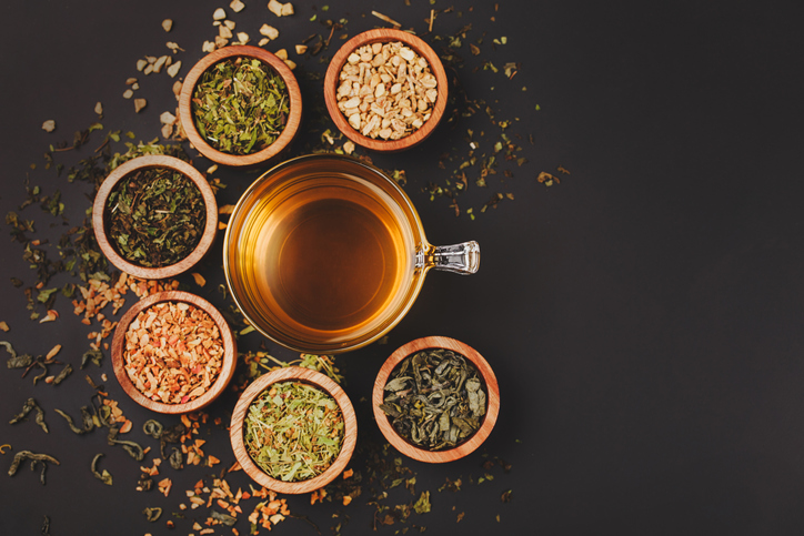 Assortment of dry tea in little bowls, on black background. Green and black tea, mint, melissa, ginger, apple, lime tree and other components for perfect beverage.