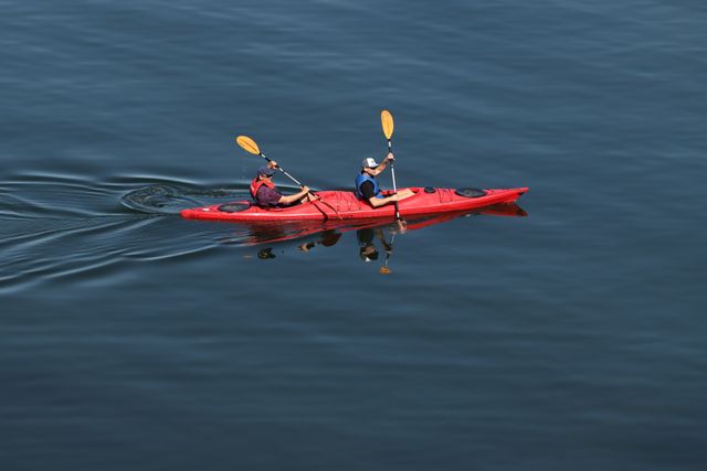 Two people kayaking in a red kayak on a serene lake