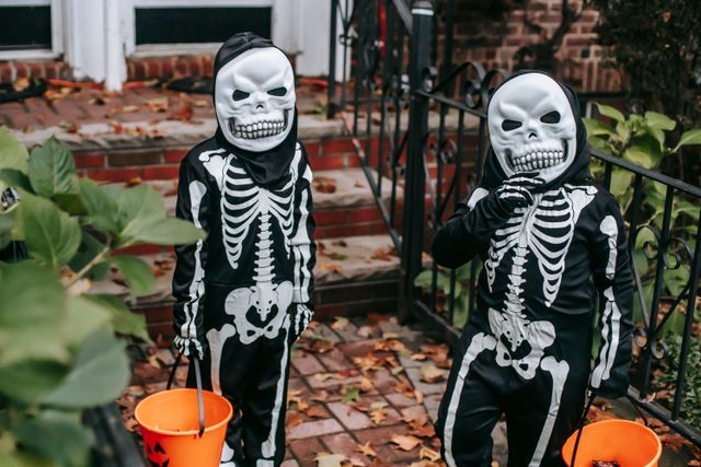 Two children in skeleton costumes with pumpkin buckets, ready for trick or treating