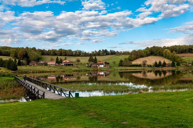 Idyllic rural landscape with a footbridge over a reflective lake and lush greenery.